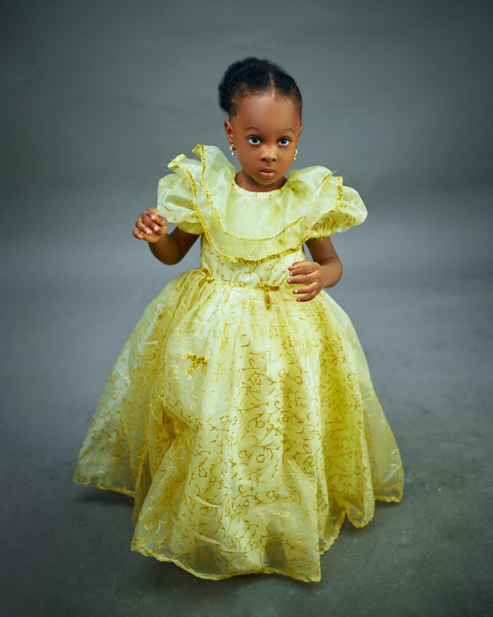 Cute young girl in a bright yellow dress with lace, posing indoors with a serious expression.